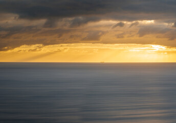 Aerial view of gold sunlight piercing through dark clouds over tranquil ocean waters, Sellicks Beach, South Australia, Australia.