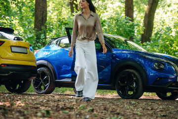 Posing for the camera. Young woman is in the forest with two cars