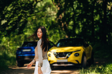 Posing for the camera. Young woman is in the forest with two cars
