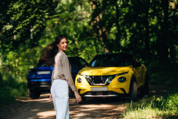 Standing and posing. Young woman is in the forest with two cars
