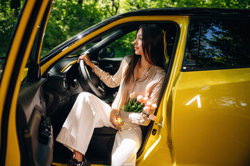 Sitting and holding flowers. Woman is with her car in the forest