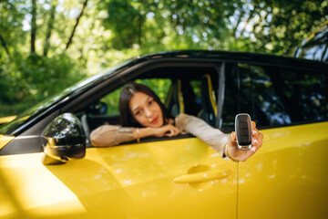 Happy owner is holding keys. Woman is with her car in the forest