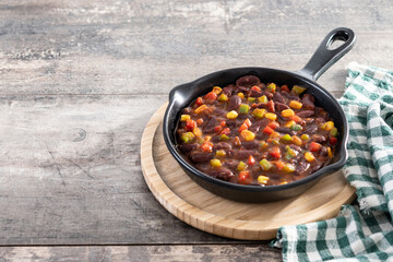 Mexican chilli beans with vegetables in iron pan on wooden table. Copy space