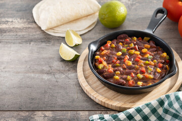 Mexican chilli beans with vegetables in iron pan on wooden table. Copy space
