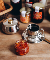 Cozy rustic breakfast table with fresh bread, citrus fruits, and assorted jam jars, half of orange and red wine glass 