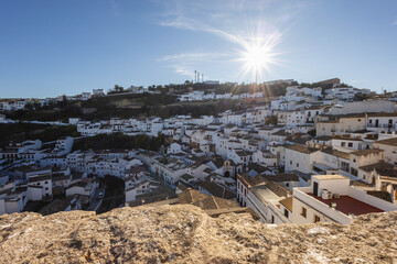View of Setenil de las Bodegas, Spain from a lookout, with a bright blue sky and sun rays radiating. A stunning landscape blending traditional architecture with natural beauty. © Juan