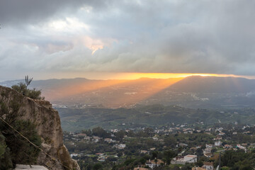 Cloudy sunset over Mijas valley, Andalucía, with sun rays breaking through clouds, casting light...