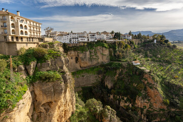 Obraz premium Sunny view of Ronda resting on a cliff, highlighting the depth and dramatic drop of the rocky gorge below. A stunning Andalusian town with breathtaking natural scenery.