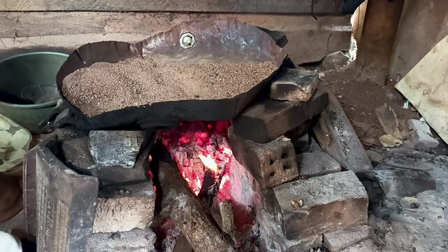 wood-burning stove, heating sand to roast melinjo fruit. a technique for frying without using oil.