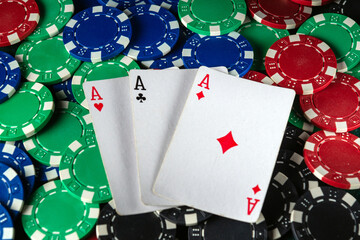 Three playing cards showing aces rest atop a vibrant mix of poker chips in various colors, creating...