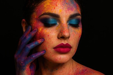 A womans face is covered in vibrant, colorful paint, creating a striking artistic makeup look