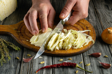 Hands skillfully slice fresh cabbage on a wooden cutting board. Nearby, spices, onion, and garlic enhance the rustic kitchen atmosphere, creating a culinary vibe filled with flavor