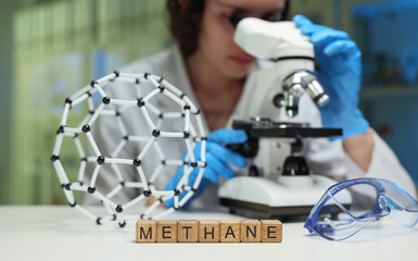 A researcher is closely examining methane using a microscope alongside a detailed 3D molecular model