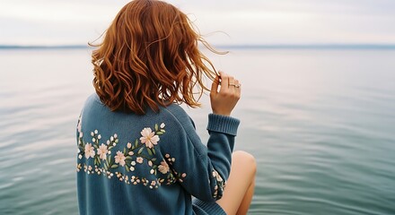 Woman by the Water in a Blue Sweater with Embroidered Floral Design