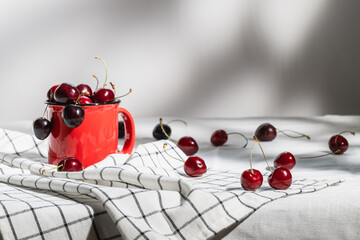 A red mug with ripe red cherries on a checkered napkin. Selective focus.
