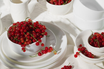 Bowls with fresh ripe red currants on a white tablecloth.