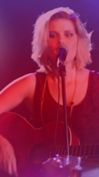 Animation of spots of light against caucasian female singer playing guitar and singing at a concert