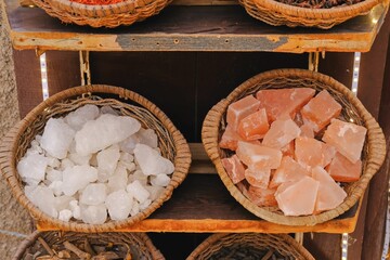 Baskets of raw Himalayan pink and white rock salt crystals on shelves at traditional market. Natural mineral products for sale in Middle Eastern souk