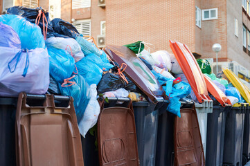 Trash bins of different colors placed on the street for neighbors to separate and recycle household waste, completely full due to a public garbage collection strike