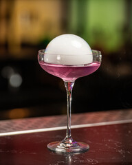 This visually striking pink alcoholic cocktail in a coupe glass features a large, dome-shaped smoke bubble on top, with more smoke billowing around it