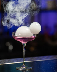 This visually striking pink alcoholic cocktail in a coupe glass features a large, dome-shaped smoke...