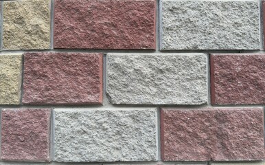 Decorative wall of rectangular stone blocks in warm shades of yellow, gray, and red — textured...