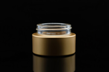 Empty gold cosmetic jar with glass opening on black background