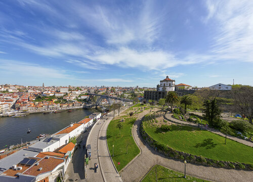 Aerial view of Dom Lu&Atilde;&shy;s I Bridge spanning the Douro River, blending with the terracotta rooftops and the verdant Jardim do Morro under a vast, bright sky, Porto, Porto District, Portugal.