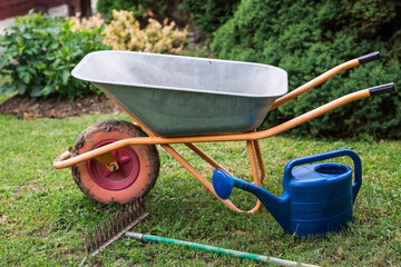 A garden wheelbarrow, rake, and watering can in the backyard of a house. The concept of gardening...