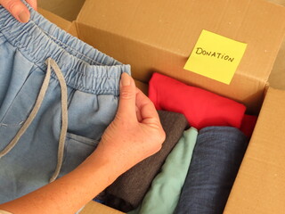 Woman hands preparing a box of clothes for donation. Hands holding a child short. Sorting clothes...
