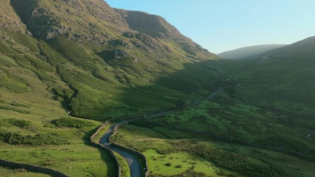 Car heading up winding mountain road at sunrise. Summer. Kirkstone Pass, Lake District, Cumbria, UK.