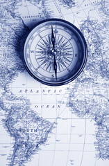 A vintage compass rests atop a detailed world map, evoking exploration and navigation.