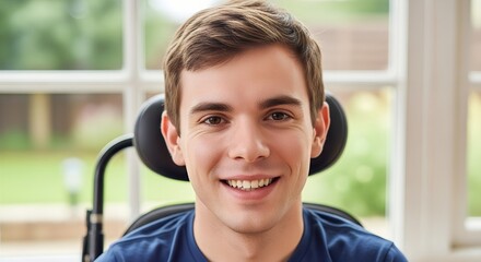 Young man in wheelchair smiling indoors by large window  