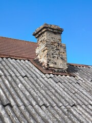 Weathered asbestos roof with aged brick chimney. Rustic, timeworn building elements symbolizing...