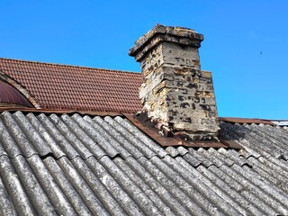 Weathered asbestos roof with aged brick chimney. Rustic, timeworn building elements symbolizing...