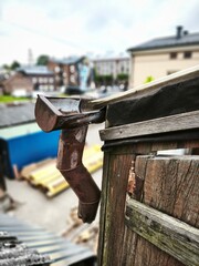 Close-up of a rusty broken drainpipe on a weathered wooden building, with an industrial urban...