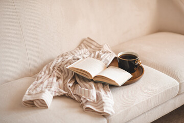 Cup of black tea with open paper book and pajamas shirt cloth on wooden tray in couch in living room close up. Good morning. Breakfast time.