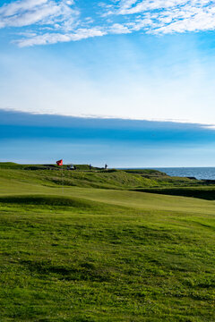 View of vivid green golf course meets the rugged coastline under a vast blue sky with scattered clouds, Vestmannaeyjab&Atilde;&brvbar;r, Vestmannaeyjab&Atilde;&brvbar;r, Iceland.