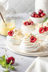 Meringues mini pavlova cakes with whipped cream decorated with fresh cherry berries and mint leaves on white marble background. Light summer dessert