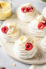 Meringues mini pavlova cakes with whipped cream decorated with fresh cherry berries and mint leaves on white marble background. Light summer dessert