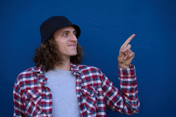 Young man pointing finger showing something interesting on blue background