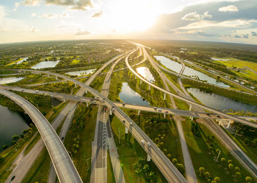 Aerial view of a complex interchange of roads and highways reflecting the sunset, cutting through the lush green landscape, Sunrise, Florida, United States.