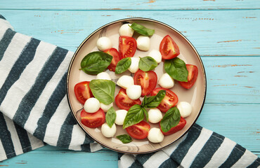 Italian Caprese salad with cherry tomatoes, mozzarella, basil on plate on blue wooden background.