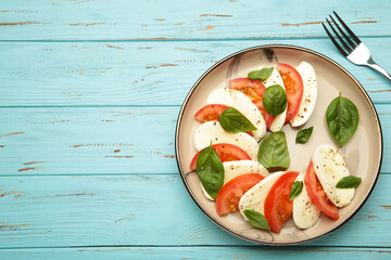 Italian Caprese salad with cherry tomatoes, mozzarella, basil on plate with fork on blue wooden background.