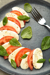 Italian Caprese salad with cherry tomatoes, mozzarella, basil on plate with fork on blue wooden background.