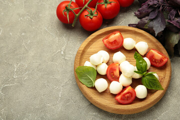 Italian Caprese salad with cherry tomatoes, mozzarella, basil on plate on grey concrete background. Space for text