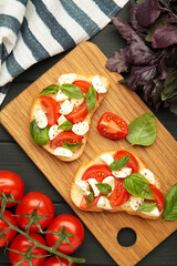 Tasty sandwich with mozzarella cheese, tomatoes and basil on cutting board on black wooden background. Caprese