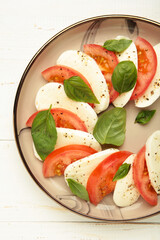 Italian Caprese salad with cherry tomatoes, mozzarella, basil on plate on white background.