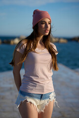 Fashion model posing on pier, wearing pink beanie and denim shorts
