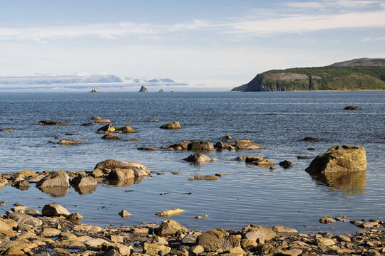 Calm seascape with rocky shore. Gertner Bay, Sea of ​​Okhotsk. In the distance, Cape Krasny (Vostochny) and rocky islands Tri Brata. Nature of Magadan Region. Russian Far East.